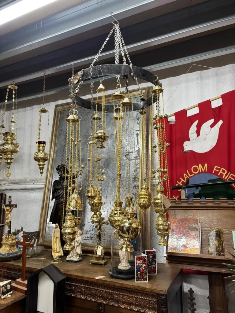 Hanging brass sanctuary lamps and censers above a table of religious figures, with a red church banner bearing a white dove