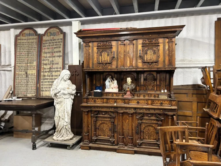 A large carved oak dresser beside a white statue of the Madonna and Child and a pair of painted Commandment boards