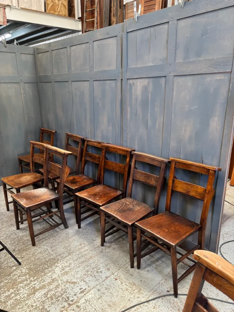 A row of antique wooden chapel chairs lined up against painted church panelling