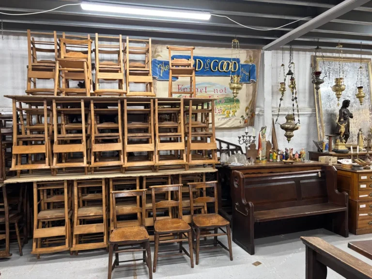 Chapel chairs stacked high against the wall beside a painted church banner and hanging brass sanctuary lamps