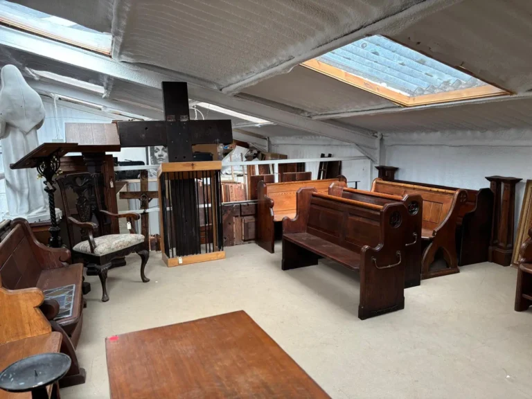 Church pews, a prayer desk and a carved armchair lit by a skylight on the warehouse floor