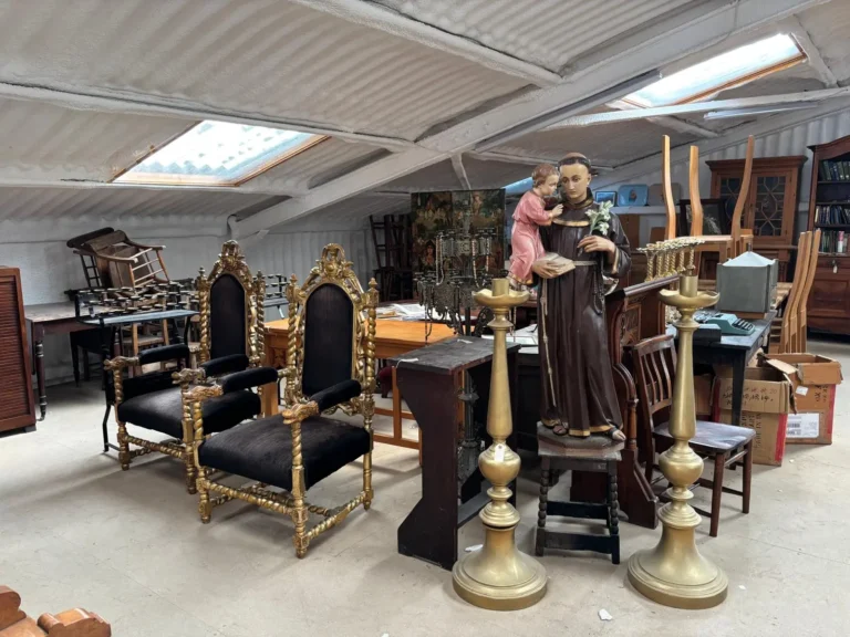 A pair of gilded carved throne chairs, tall brass altar candlesticks and a painted statue of a saint holding the Christ Child
