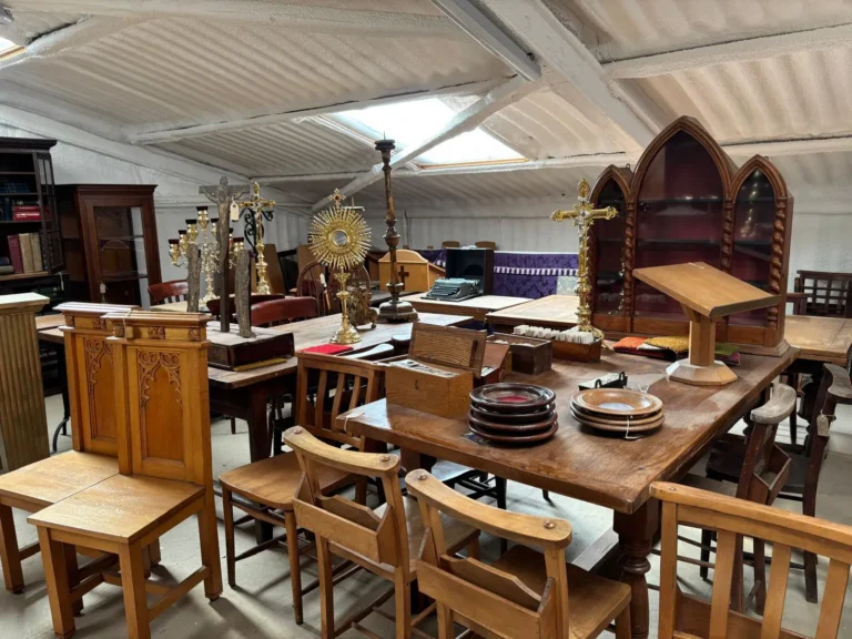 Oak chapel chairs and tables beneath a gothic arched cabinet, with a gilt monstrance, a crucifix and a reading desk