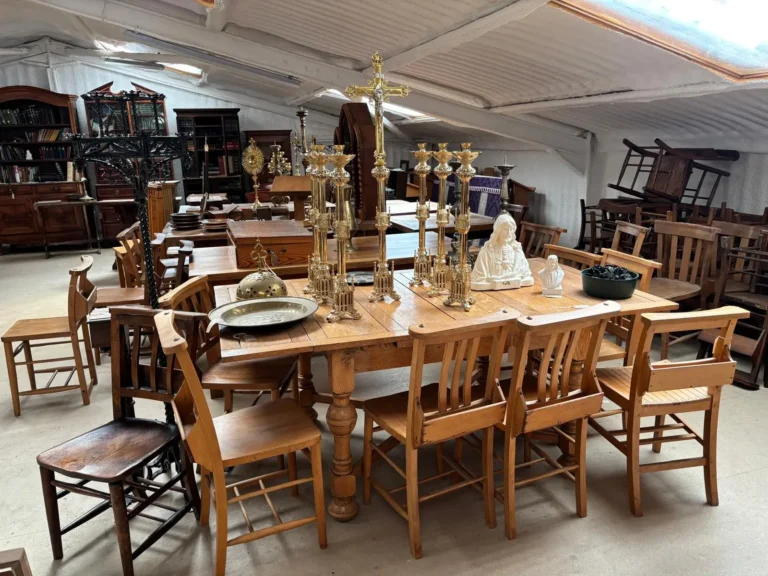A pine refectory table set with brass altar candlesticks, a crucifix and alms dishes, surrounded by chapel chairs