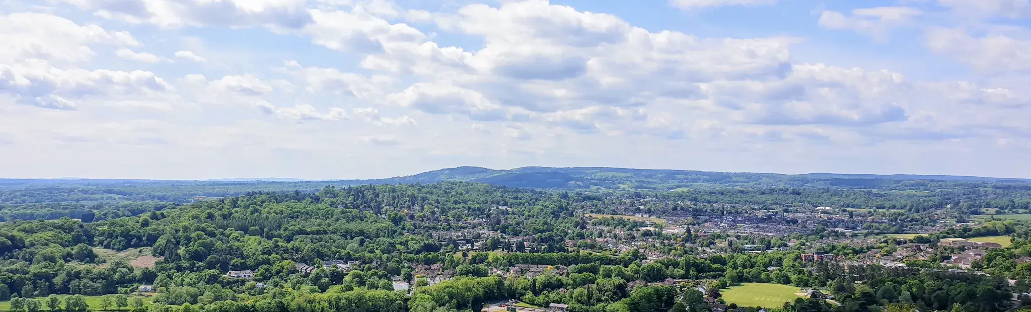 Looking out from Box Hill across woodland and the town of Dorking to the Surrey Hills, under a summer sky