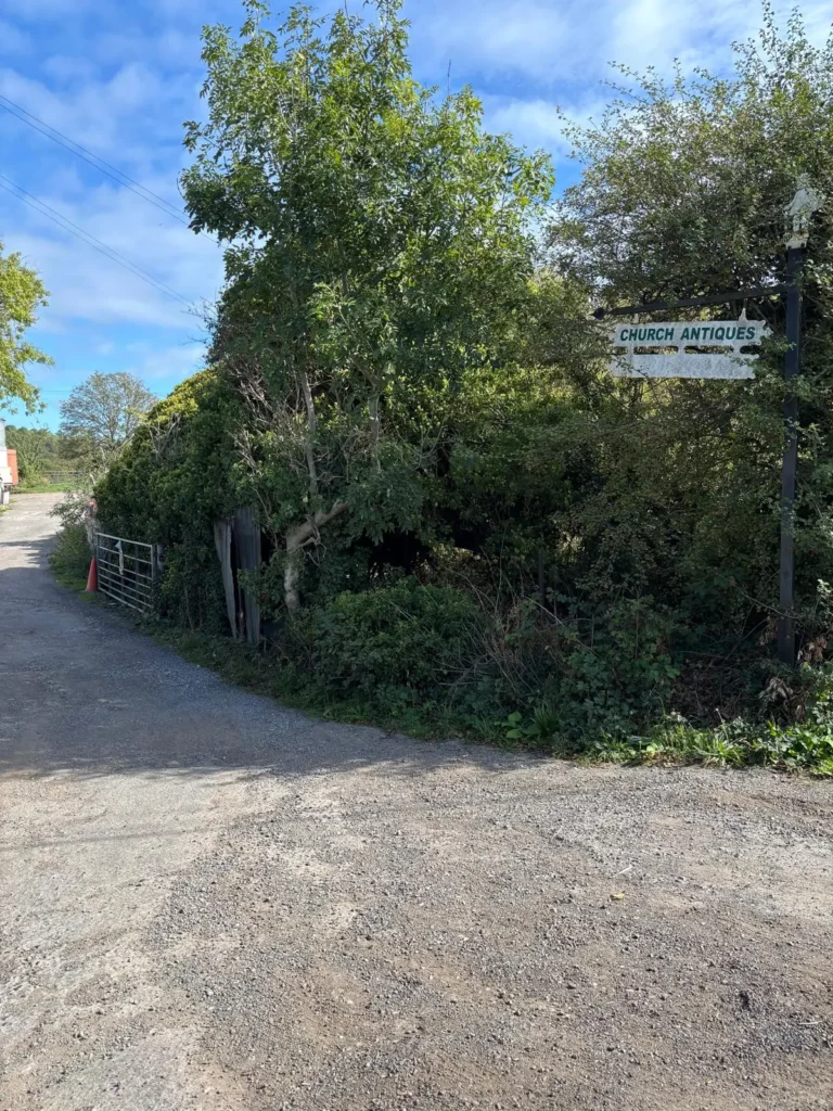 A gravel farm track with a white fingerpost sign reading Church Antiques, marking the way in to Fryleigh Farm Barn in Betchworth