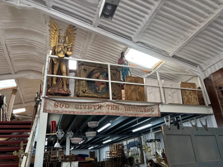 A gilded winged angel and a framed Madonna and Child along the mezzanine rail, above a painted banner reading God Giveth the Increase
