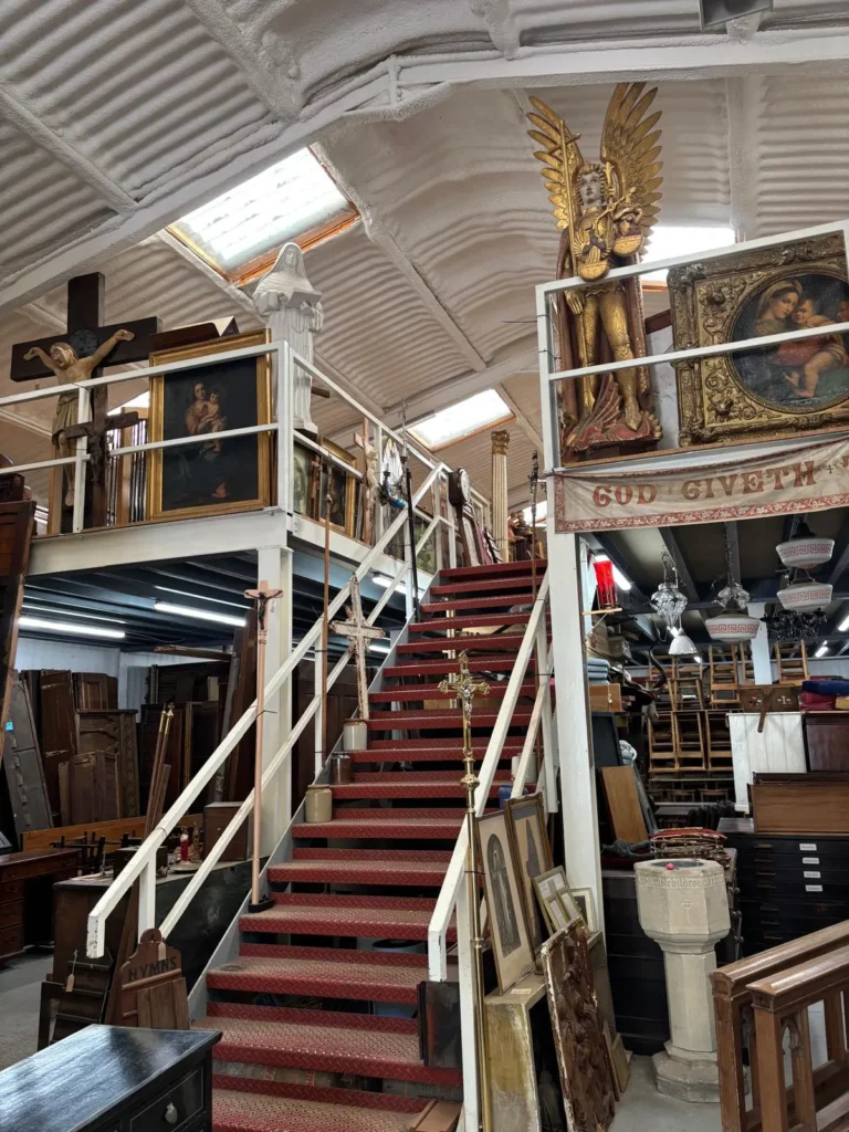 Red carpeted staircase leading up to the mezzanine, with a gilded angel, religious paintings and a crucifix along the rail