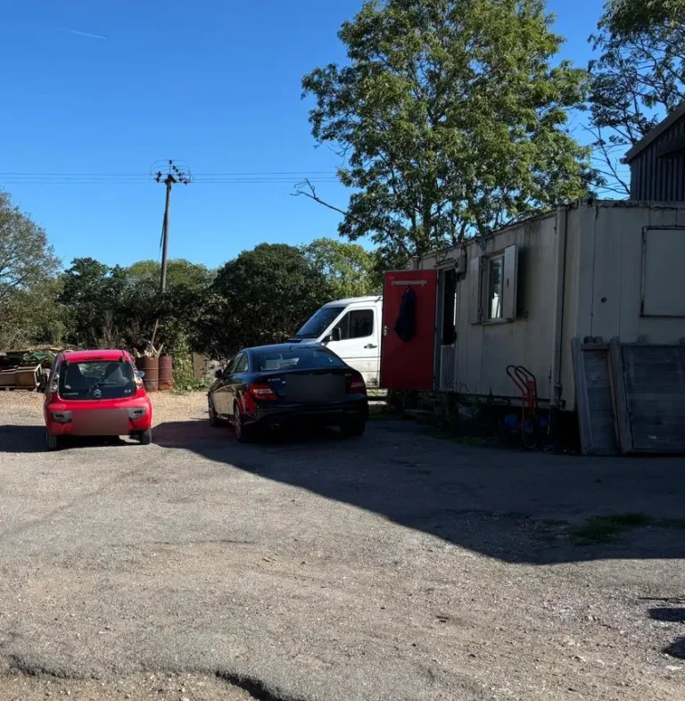The office portacabin with its red door and the warehouse beyond, on the far side of the yard at Fryleigh Farm Barn, with cars parked in front