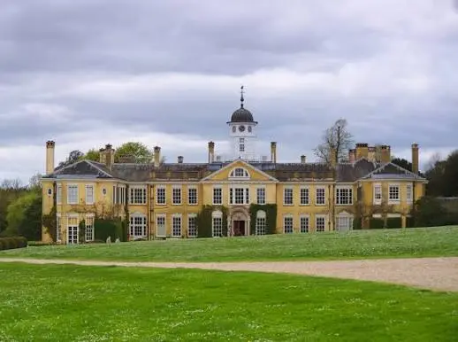 Polesden Lacey, a yellow Edwardian country house with a clock tower, seen across the lawns